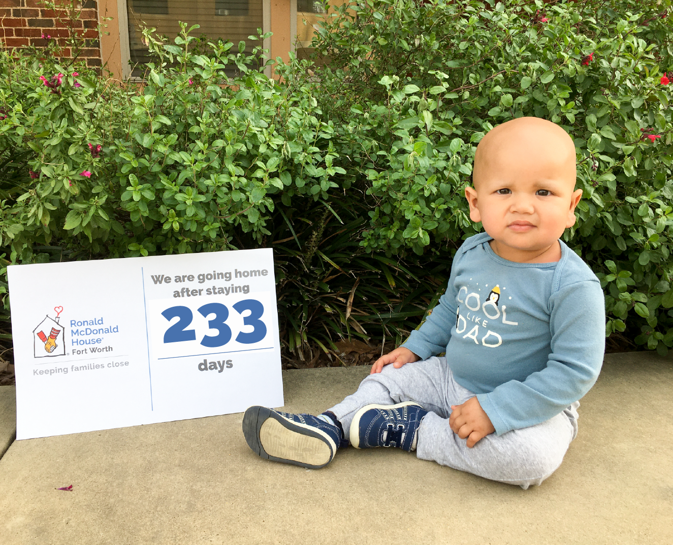 Baby sitting next to a sign that says they are going home after 233 days of staying at RMHFW