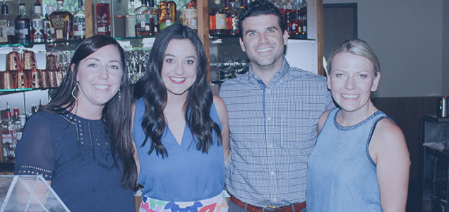Three women and one man standing in front of a bar cabinet